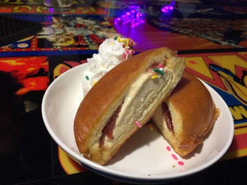 A plate with two split doughnuts filled with ice cream and strawberry sauce, topped with whipped cream and sprinkles.