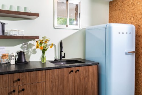 A modern kitchen with a blue SMEG fridge, wooden cabinets, a black countertop, and a vase of flowers.