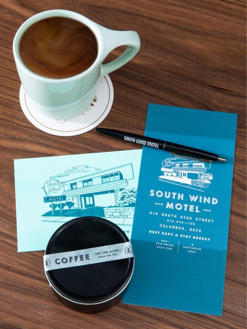 A coffee cup, a pen, and promotional materials for South Wind Motel on a wooden table.