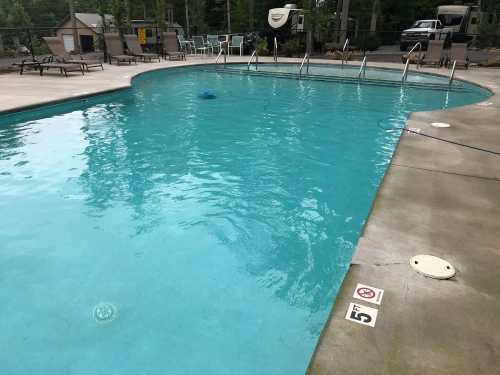 A clear swimming pool surrounded by lounge chairs and trees, with a no diving sign on the edge.