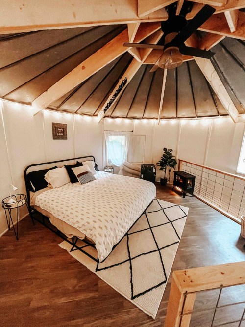 Cozy yurt interior featuring a large bed, wooden accents, and warm lighting, with a rug and plants for decor.