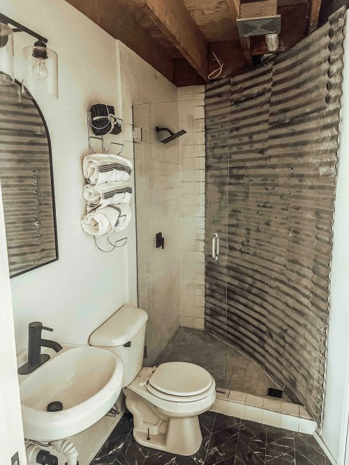 A modern bathroom featuring a glass shower, toilet, sink, and neatly arranged towels on a wall rack.
