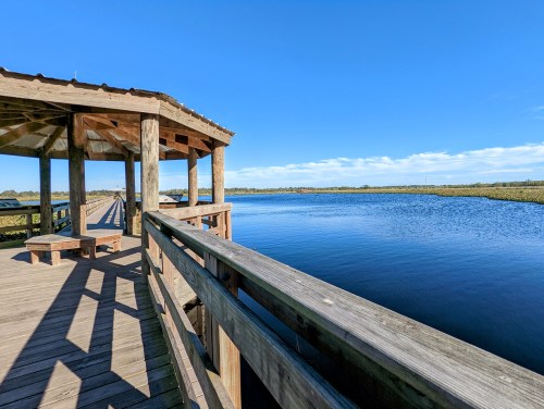 A wooden observation deck overlooking a calm river under a clear blue sky, surrounded by lush greenery.