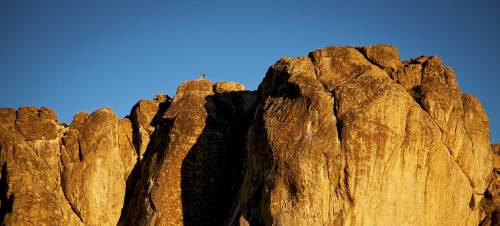 A rugged rock formation under a clear blue sky, illuminated by warm sunlight.