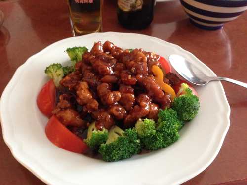 A plate of sweet and sour chicken with broccoli, bell peppers, and tomatoes, garnished with a spoon.