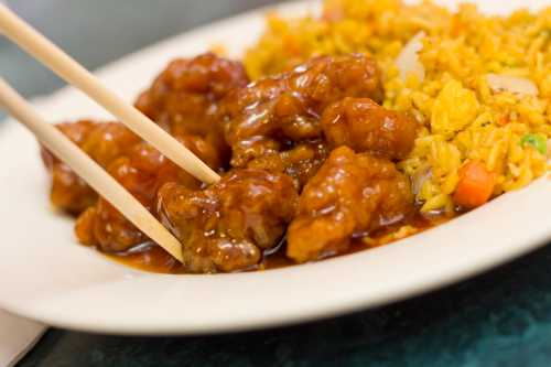 A plate of orange chicken with chopsticks, served alongside fried rice.