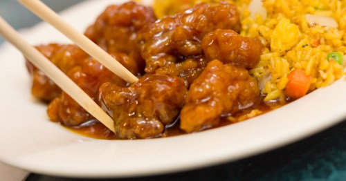A plate of orange chicken with chopsticks, served alongside fried rice with vegetables.
