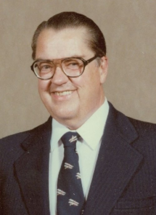 A smiling man in a suit and tie with glasses, posing against a neutral background.