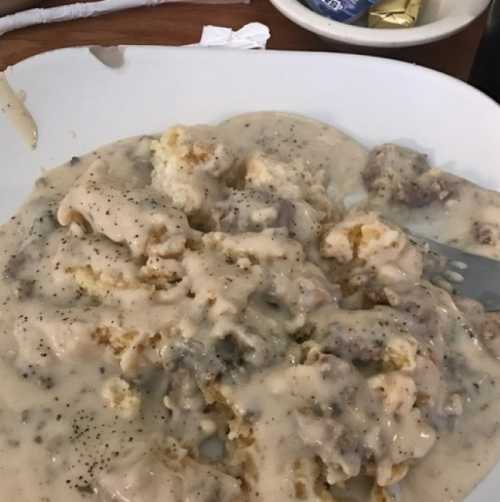 A plate of biscuits smothered in creamy sausage gravy, with a sprinkle of black pepper on top.