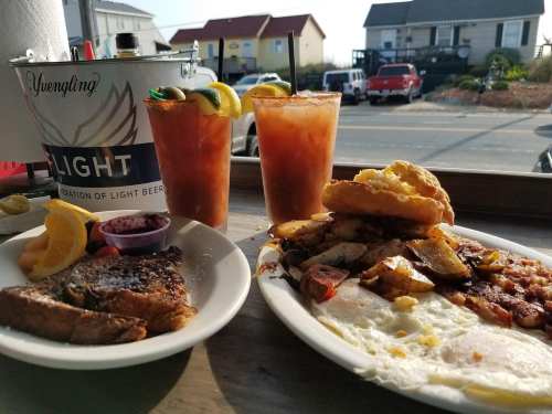 A plate of breakfast with eggs, potatoes, and French toast, alongside two drinks and a bucket of beer in the background.
