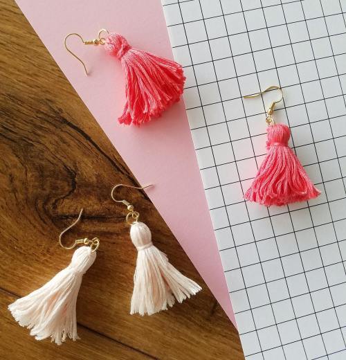 Two pairs of colorful tassel earrings in pink and light pink, displayed on a grid and pink background.