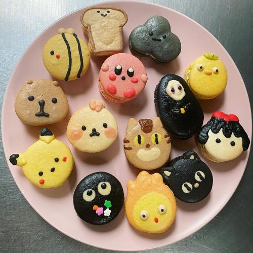 A colorful assortment of cute, themed macarons arranged on a pink plate, featuring various cartoonish designs.