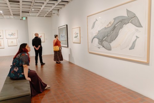Visitors admire a large whale painting in an art gallery, with various artworks displayed on the walls.