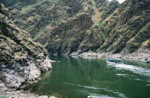 A boat navigates a serene river surrounded by steep, rocky cliffs and lush greenery.