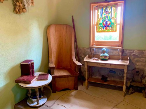 A cozy corner with a wooden chair, a small table, books, and a stained glass window illuminating the space.
