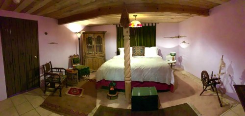 Cozy bedroom with a four-poster bed, wooden furniture, and warm lighting in a softly colored room.