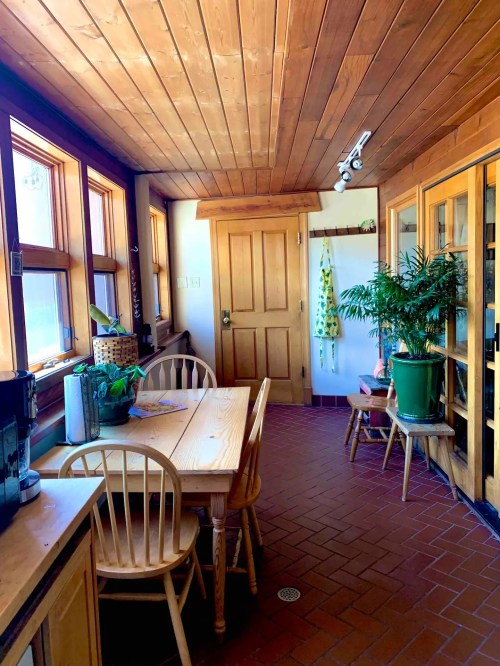 Bright, wooden kitchen with a table, chairs, plants, and large windows, creating a warm, inviting atmosphere.