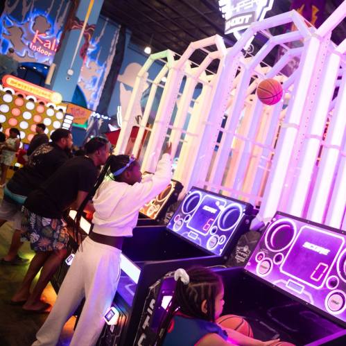A vibrant arcade scene with players enjoying a basketball shooting game under colorful lights.