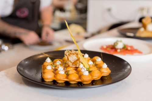 A gourmet dish featuring a waffle-like base topped with cream and a decorative garnish on a black plate.