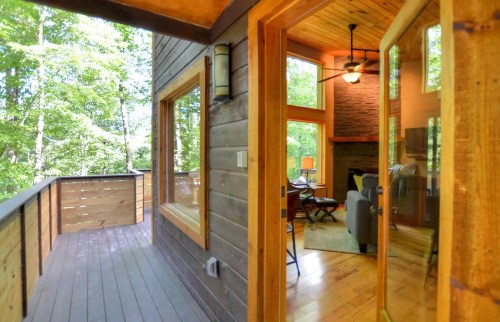 A cozy wooden interior with large windows, leading to a deck surrounded by trees. Bright and inviting atmosphere.
