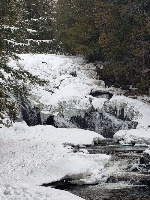 A frozen waterfall surrounded by snow-covered rocks and trees, creating a serene winter landscape.