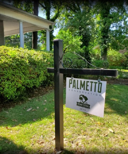 Sign for Palmetto Conservation, featuring a logo and text, set in a green outdoor area with trees and shrubs.