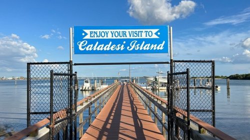 Sign welcoming visitors to Caladesi Island, with a wooden pier extending over calm waters under a blue sky.
