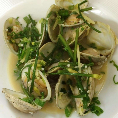 A plate of clams cooked with green onions and herbs in a light broth.