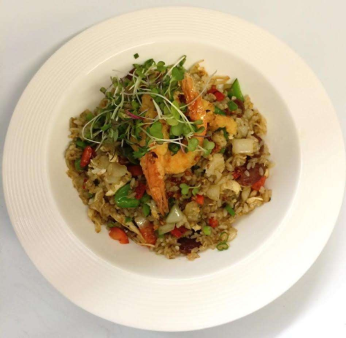 A plate of shrimp fried rice topped with microgreens and colorful vegetables.