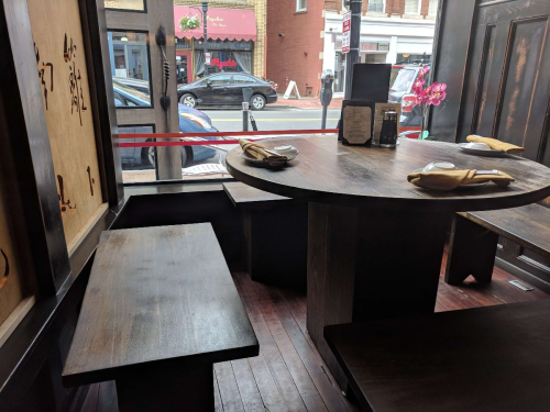 Interior of a restaurant featuring a round table, benches, and a view of the street through large windows.