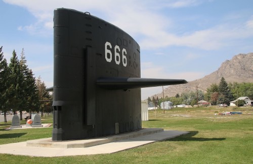 A large black submarine display with the number 666, set in a grassy area with trees and mountains in the background.