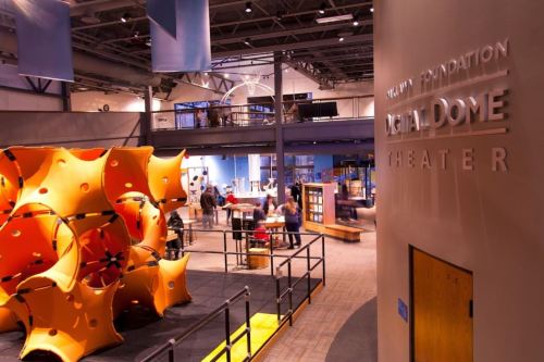 Interior of a science center featuring a colorful play structure and a digital dome theater sign. Visitors are exploring the space.