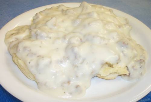 A plate of biscuits smothered in creamy sausage gravy, served on a blue tablecloth.
