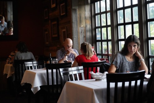 A cozy restaurant scene with diners at tables, featuring a man and woman deep in conversation and a woman looking contemplative.