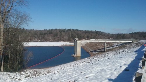A snowy landscape with a reservoir, a dam structure, and a clear blue sky in the background.