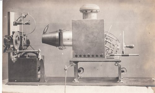 A vintage machine with a large metal body, a funnel-shaped front, and various mechanical components on a wooden base.