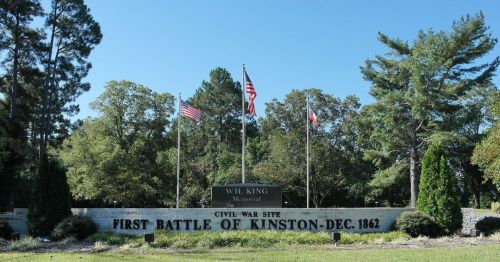Sign marking the First Battle of Kinston, December 1862, with flags and trees in the background.