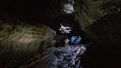 A group of people exploring a dark cave with rocky terrain and a beam of light shining through an opening above.
