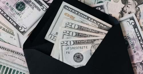 An envelope containing several twenty-dollar bills on a background of various U.S. banknotes.
