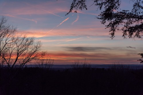 A serene sunset over a landscape, with colorful clouds and silhouetted trees in the foreground.