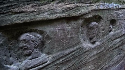 Carved stone reliefs depicting human faces on a textured rock surface.