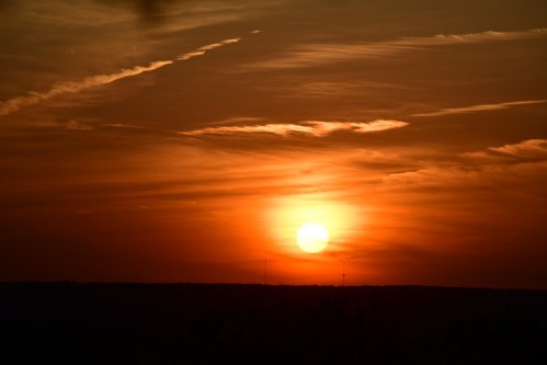A vibrant sunset with orange and yellow hues, casting a warm glow over the horizon and silhouetting distant land.
