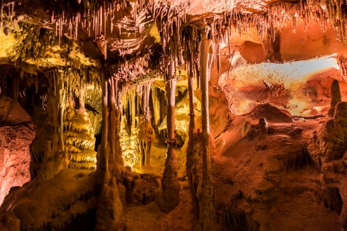 A colorful cave interior with stalactites and stalagmites illuminated by warm lighting.