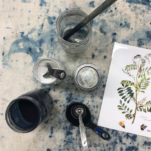 A flat lay of jars, measuring spoons, and a botanical illustration on a textured blue background.