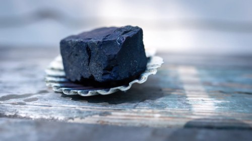 A dark, textured block of material resting on a decorative shell-shaped dish on a weathered wooden surface.