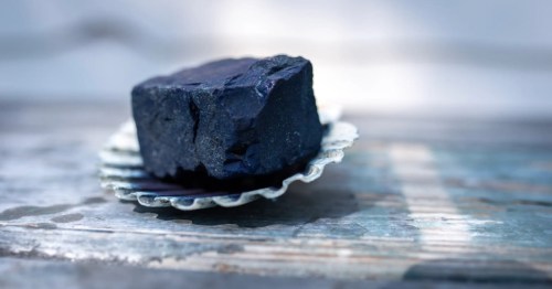 A piece of black coal resting on a scalloped shell on a weathered wooden surface.