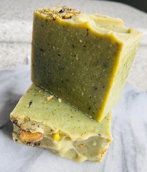 Two stacked bars of green soap with visible herbs and natural ingredients on a marble surface.
