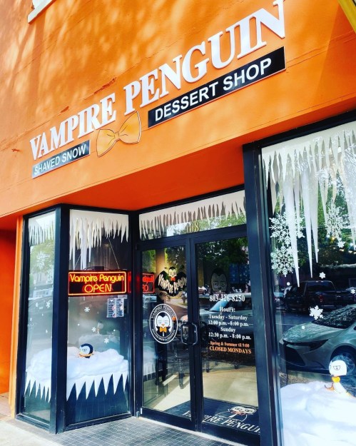 Exterior of Vampire Penguin dessert shop, featuring a bright orange facade, snow-themed decor, and an "OPEN" sign.