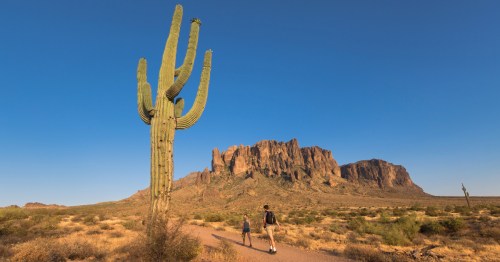 two hikers out on a desert trail with the superstition mountains in the background at lost dutchman state park in arizona