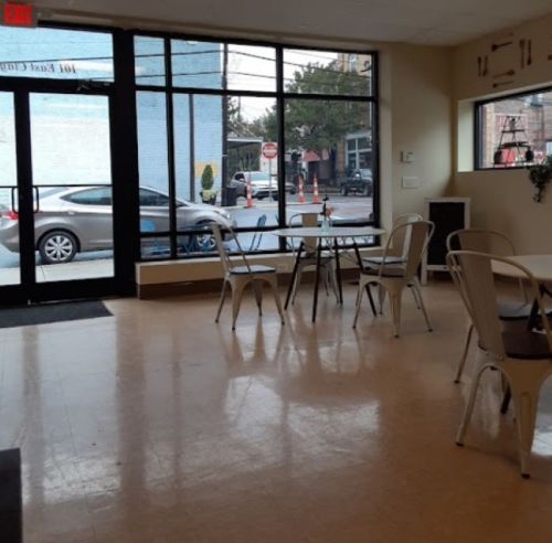 Interior of a cafe with empty tables and chairs, large windows showing a street view outside.